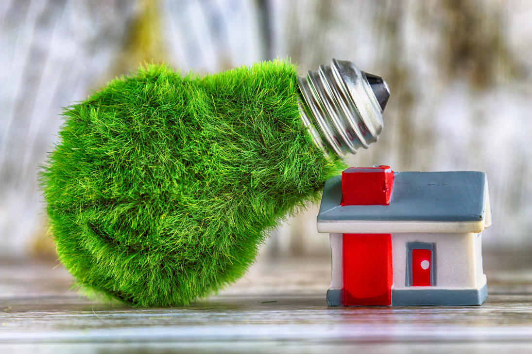 Green eco light bulb with grass and miniature house. Renewable energy concept. Electricity prices, energy saving in the household.